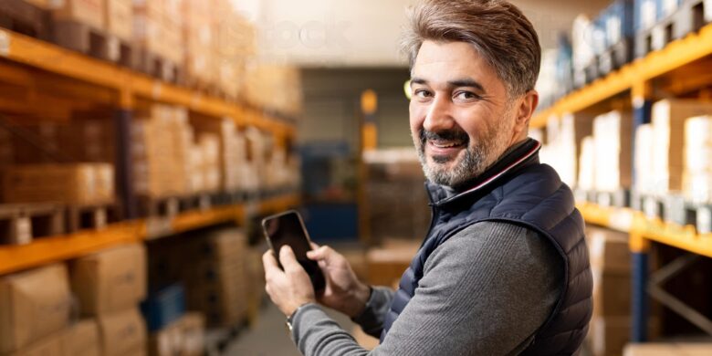 Homem com celular na mão no estoque.